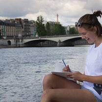 High School Semester Abroad! girl writing on paper sitting next to river